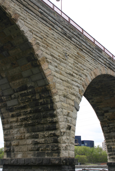 Pedestrians strolling across the historic Stone Arch Bridge above St. Anthony Falls on a sunny Minneapolis riverfront afternoon