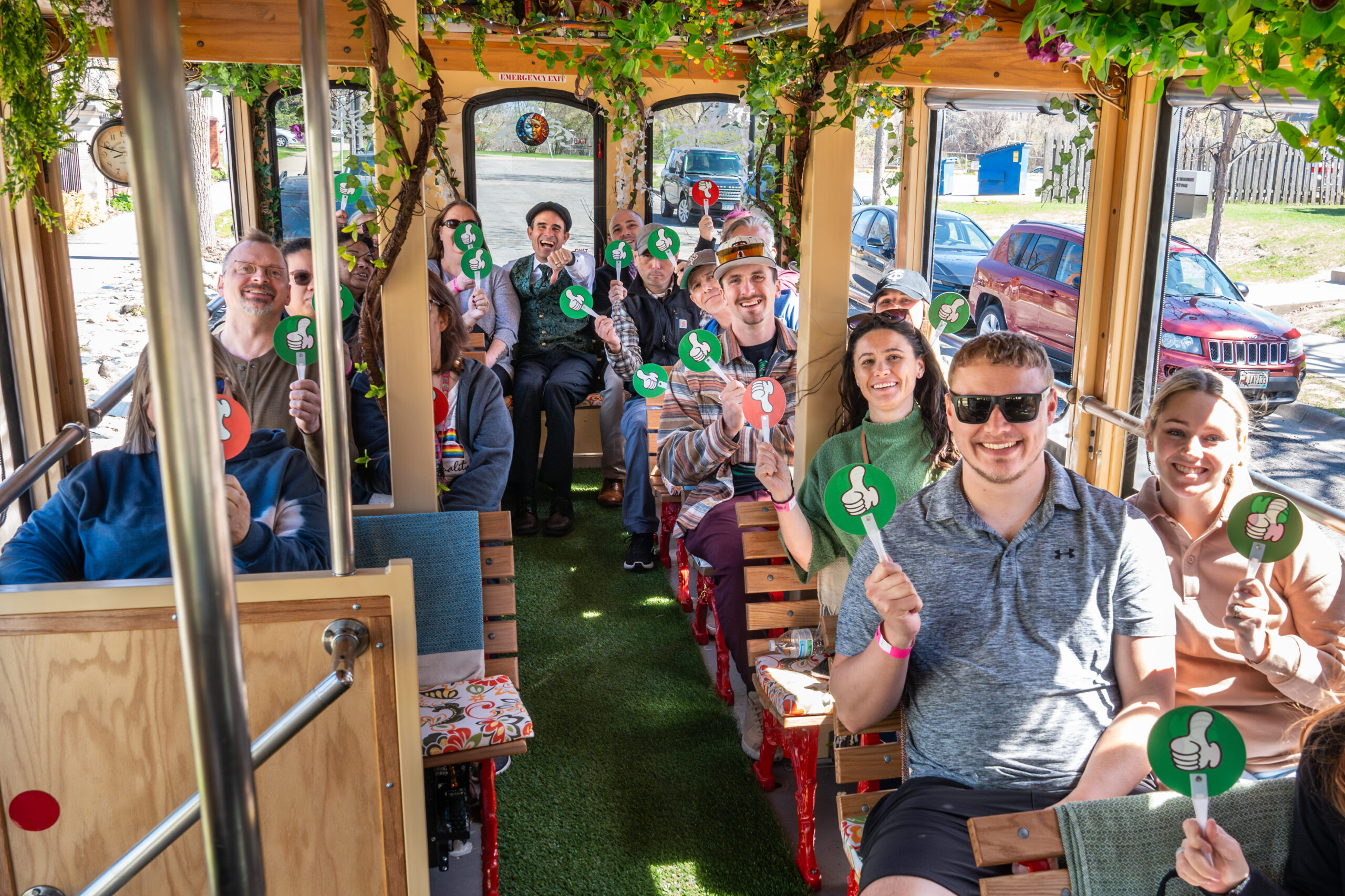 Passengers seated along the wooden benches inside a Minneapolis Trolley holding voting paddles during the True Crime tour, the open windows framing the street outside