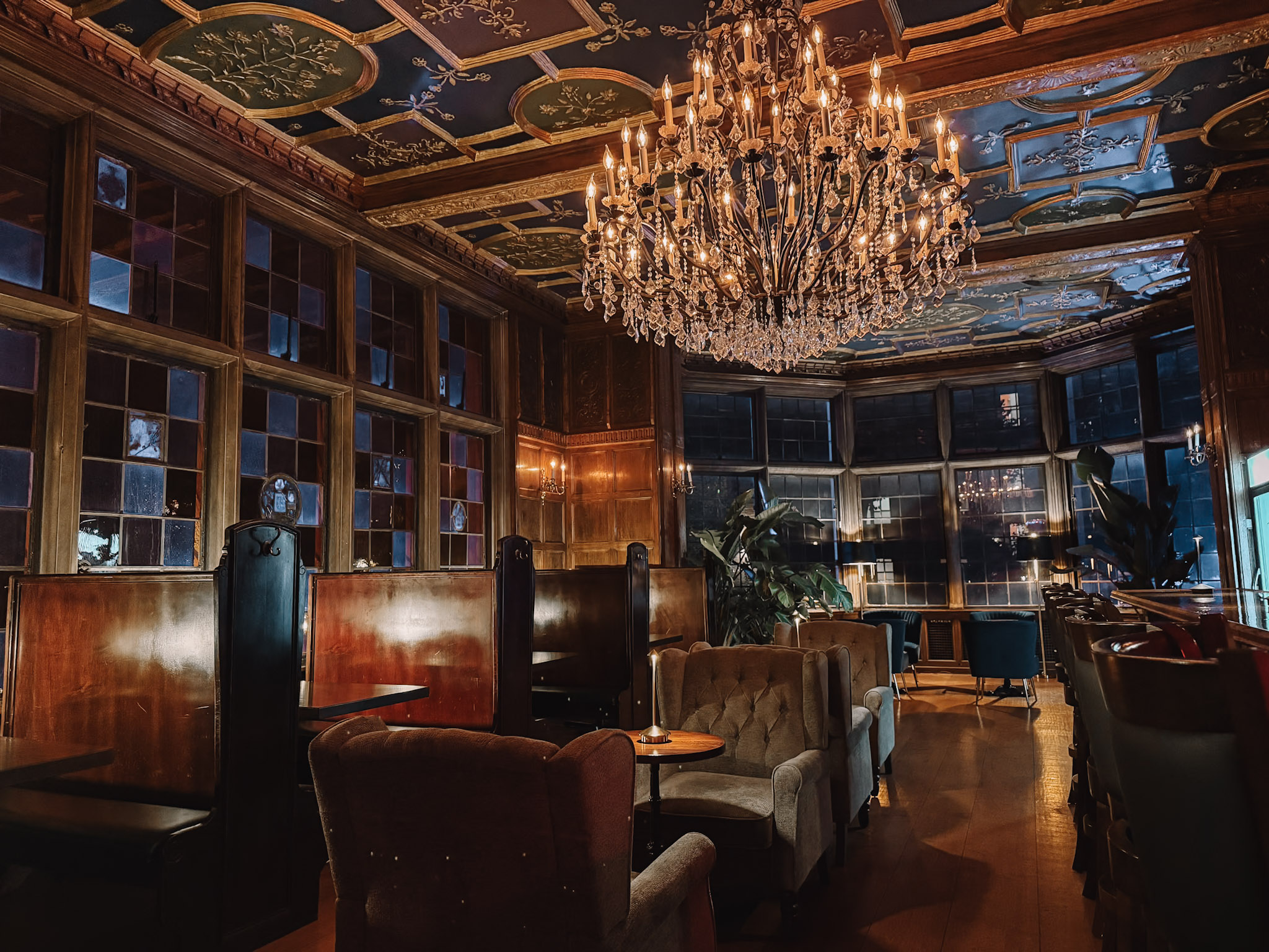 A dark wood-paneled club room inside the Pillsbury Mansion in Minneapolis lit by a crystal chandelier, with leather seating and carved English Gothic detailing